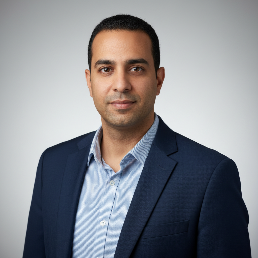 מודל גבר, הבעה בטוחה ונינוחה; לבוש בלייזר כחול כהה וחולצה מכופתרת פסים עדינה בגווני תכלת-לבן, פתוחה בצווארון; רקע אפור-בהיר מטושטש עם מעבר גוונים עדין; תאורה קדמית רכה, אווירה מקצועית ונגישה.התמונה תכיל רק אדם אחד.